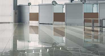 Interior of a large modern building with a shiny, reflective floor and a row of booths featuring white roll-up shutter doors.