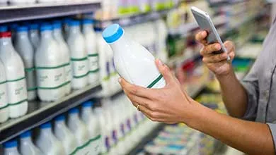 Person in a grocery aisle scanning a milk bottle with a smartphone.