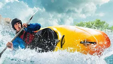 Person in helmet and blue jacket kayaks yellow and orange boat through turbulent white water.