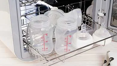 Clean baby bottles, nipples, and parts rest on a metal rack pulled out from a white sterilizer.