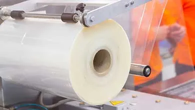 Close-up of a large roll of clear plastic film being fed into an industrial packaging machine.