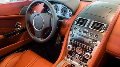 Driver’s side interior of a luxury sports car with reddish-brown leather seats, a black steering wheel, and a silver-trimmed center console.