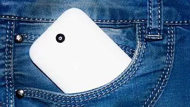 A white smartphone with a visible rear camera partially tucked into the back pocket of blue denim jeans.
